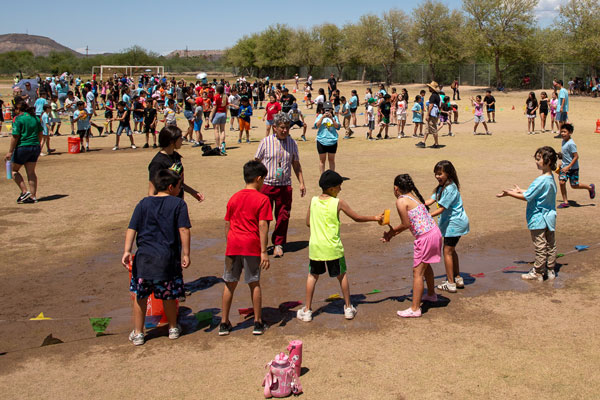 Children gather and relay over wet ground.