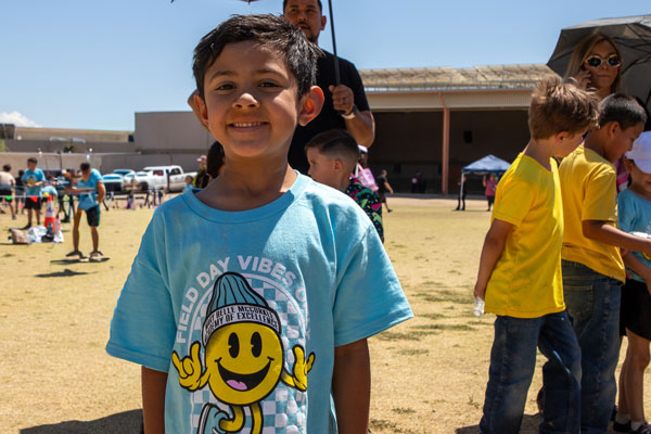 Child wears the T-shirt, Field Day Vibes, with a yello smiley face charater wearing a cap.