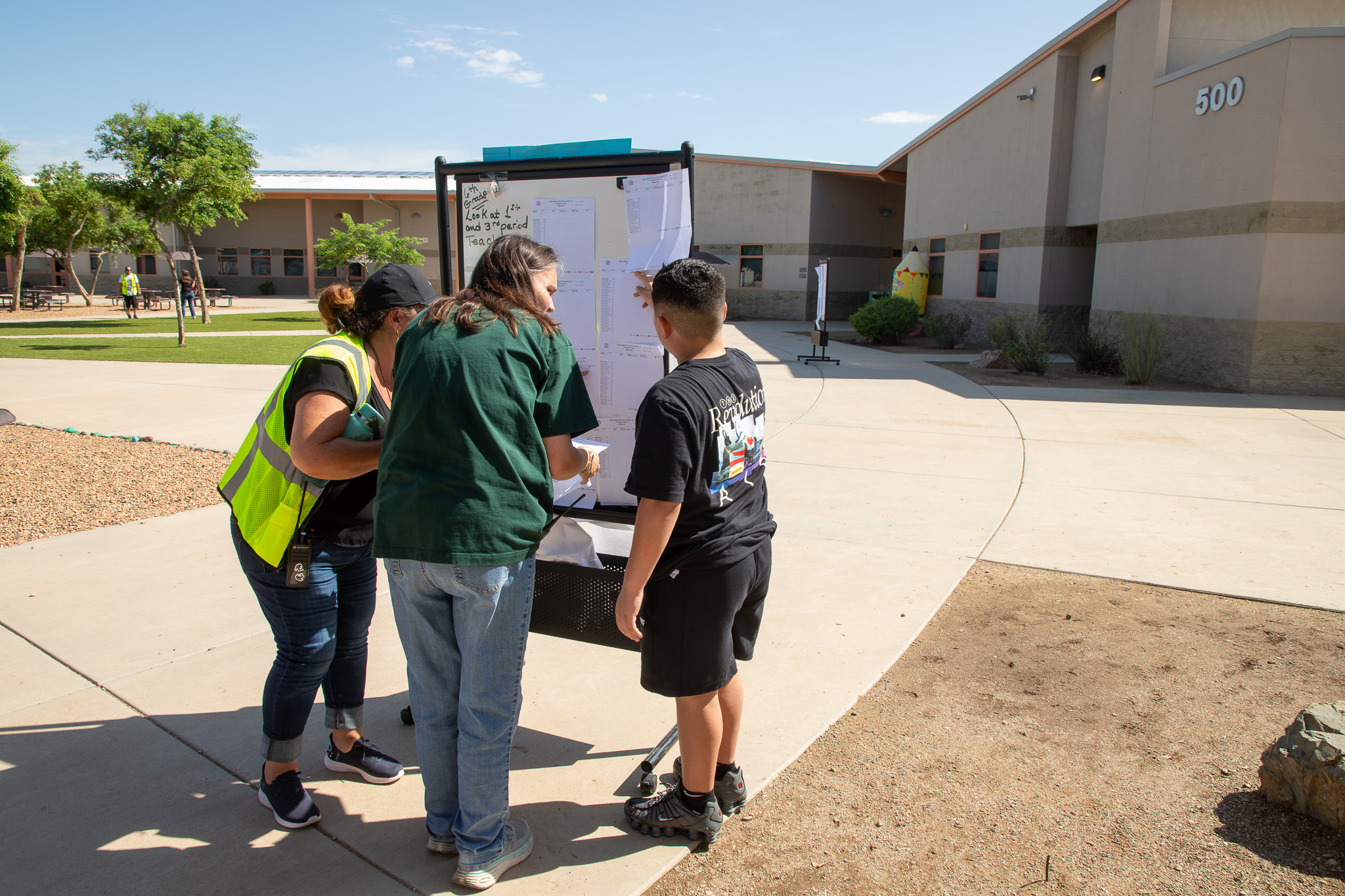 Two staff members help a boy navigate his class schedule as he stands outside the school